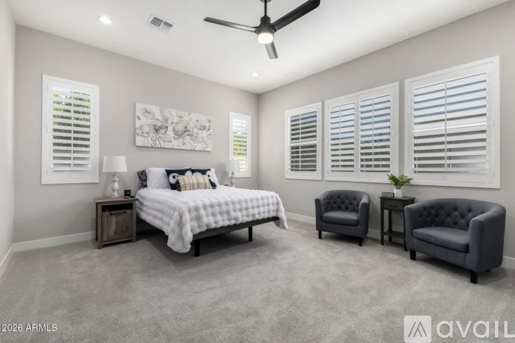 A bedroom with a bed, two chairs, and a ceiling fan.