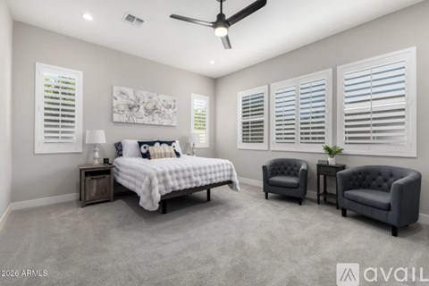 A bedroom with a bed, two chairs, and a ceiling fan.