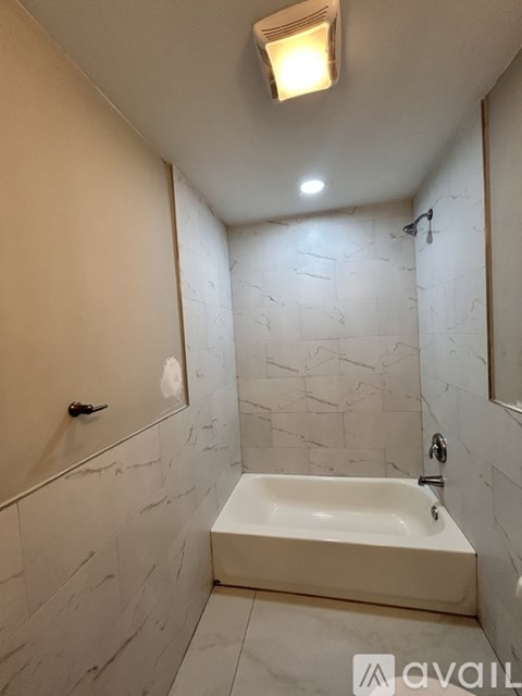 A bathroom with a marble wall and a white bathtub.