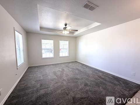 A room with a carpeted floor, a ceiling fan, and two windows.
