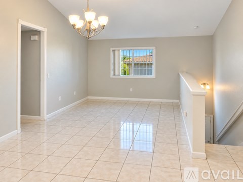 A spacious room with a chandelier, tiled floor, and a window with a view of a fence and trees.