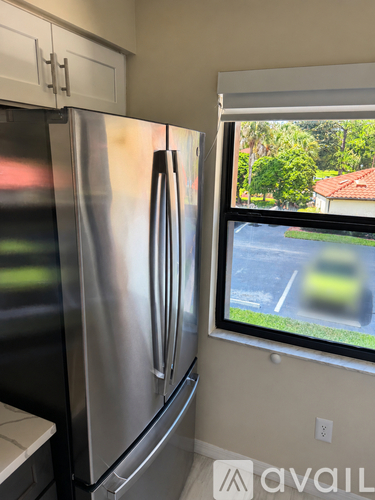 A stainless steel refrigerator in a kitchen with a window showing a blurred view of a street.