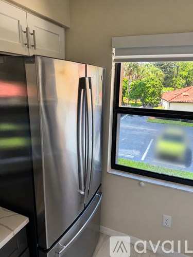 A stainless steel refrigerator in a kitchen with a window showing a blurred view of a street.