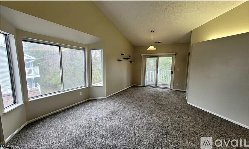 A spacious room with carpeted floor, large windows, and a door leading to another room.