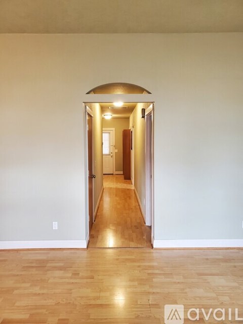 A hallway with wooden floors and white walls leading to a door.