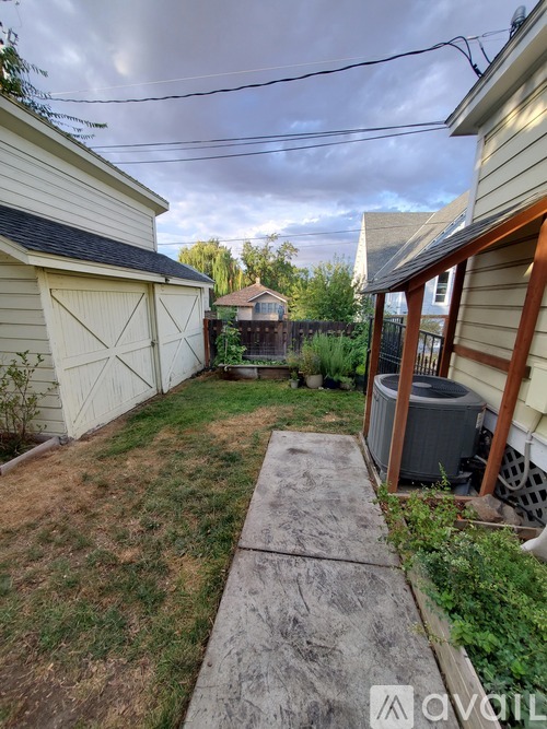 A backyard with a concrete walkway, a shed, and a house with a brown roof.