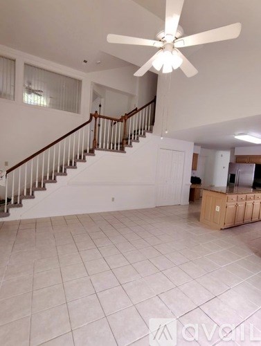 A spacious living room with a staircase and a ceiling fan.