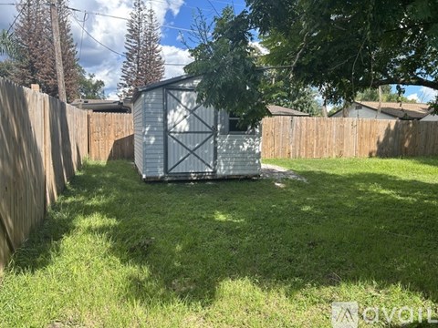 A shed sits in a backyard with a wooden fence and trees in the background.