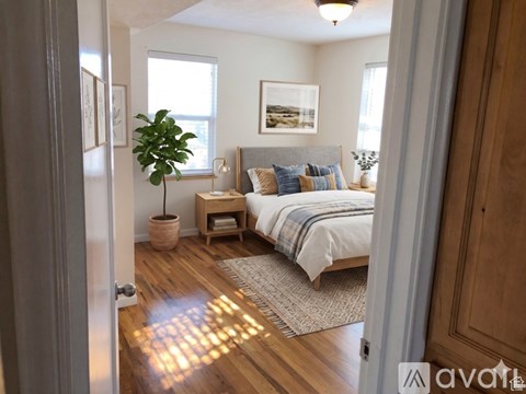 A bedroom with a bed, nightstand, and a plant.