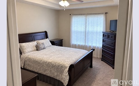A bedroom with a bed, dresser, and window with blinds.