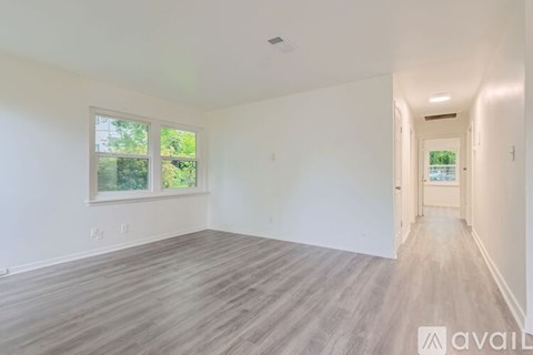 A spacious room with wooden flooring and a window overlooking greenery.