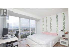 A bedroom with a bed, desk, and window overlooking a cityscape.