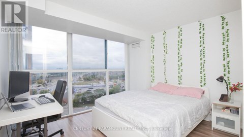 A bedroom with a bed, desk, and window overlooking a cityscape.