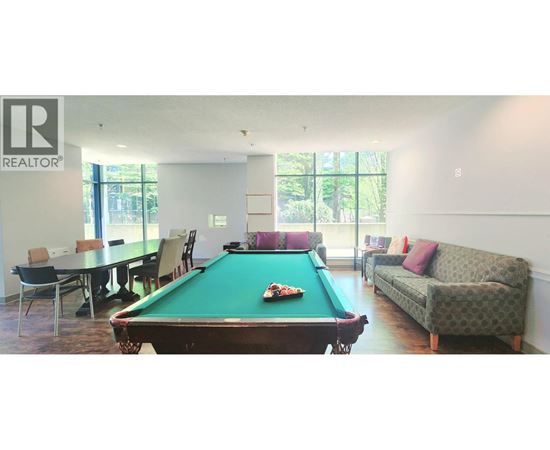 A pool table is in the middle of a room with a couch and a dining table.
