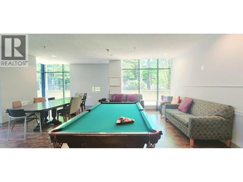 A pool table is in the middle of a room with a couch and a dining table.