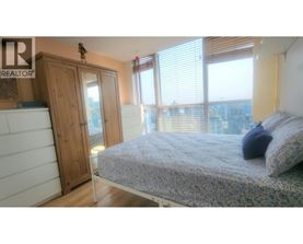 A bedroom with a bed, a wardrobe, and a window overlooking a cityscape.