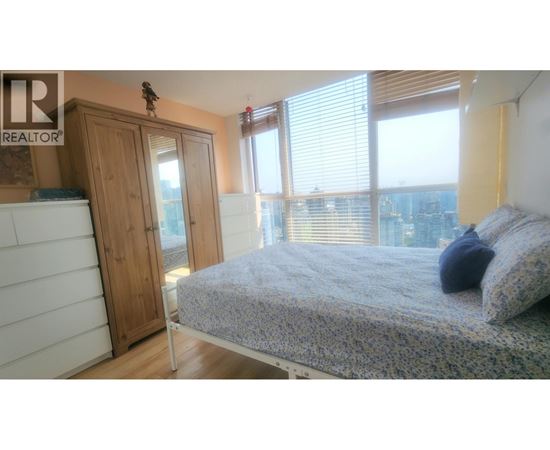 A bedroom with a bed, a wardrobe, and a window overlooking a cityscape.
