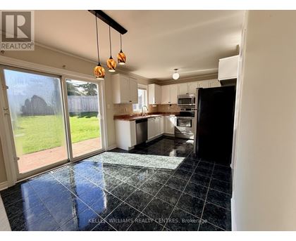 A kitchen with black tiles on the floor and a view of a backyard through the sliding glass doors.