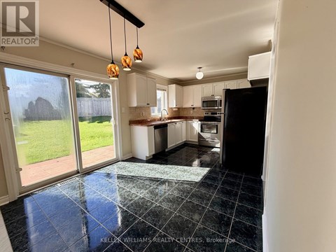 A kitchen with black tiles on the floor and a view of a backyard through the sliding glass doors.