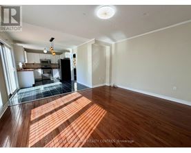 A spacious room with wooden flooring and a kitchen area in the background.