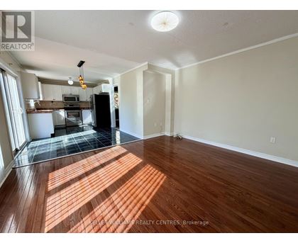 A spacious room with wooden flooring and a kitchen area in the background.