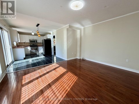 A spacious room with wooden flooring and a kitchen area in the background.