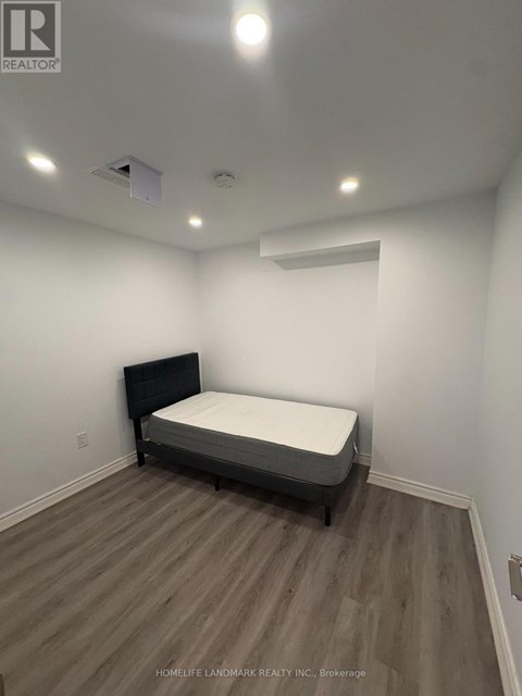 A bedroom with a bed, wooden flooring, and a ceiling light fixture.