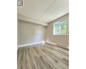A room with wooden flooring and a window showing trees outside.