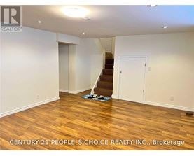 A room with wooden flooring and a staircase in the background.