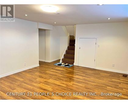 A room with wooden flooring and a staircase in the background.
