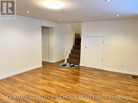 A room with wooden flooring and a staircase in the background.