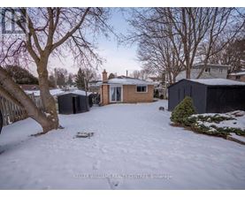 A snowy yard with a house and trees in the background.