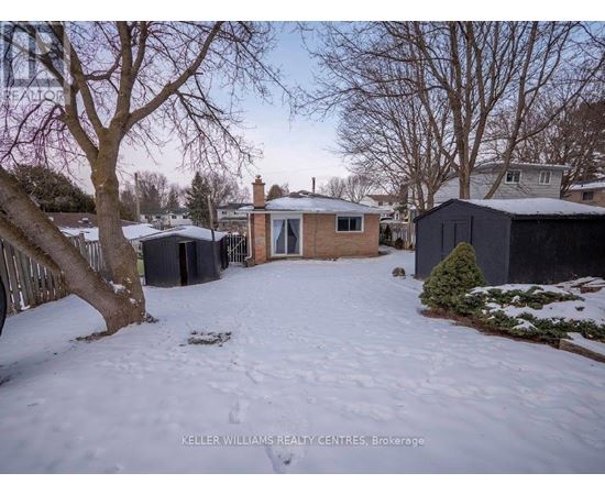 A snowy yard with a house and trees in the background.
