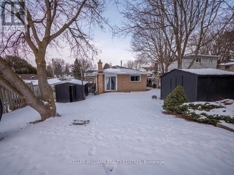 A snowy yard with a house and trees in the background.