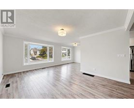 A spacious room with wood flooring and a large window showing a view of a house and trees.
