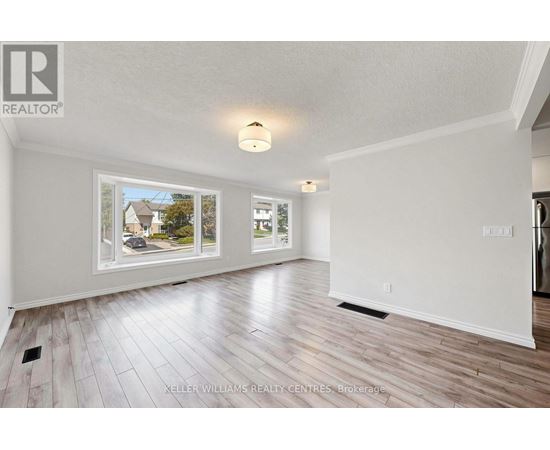 A spacious room with wood flooring and a large window showing a view of a house and trees.