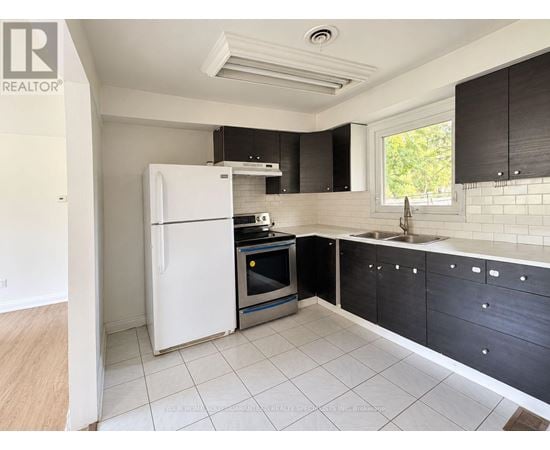 A kitchen with a white fridge, black cabinets, and a window.