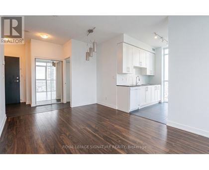 A spacious room with wooden floors and white walls, featuring a kitchen area with white cabinets and a countertop.