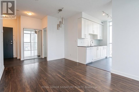 A spacious room with wooden floors and white walls, featuring a kitchen area with white cabinets and a countertop.
