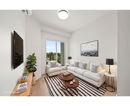 A living room with a white couch, a coffee table, and a flat-screen TV mounted on the wall.