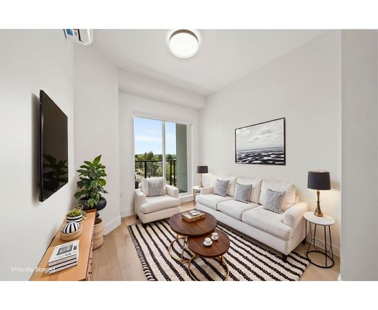A living room with a white couch, a coffee table, and a flat-screen TV mounted on the wall.