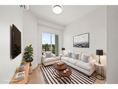 A living room with a white couch, a coffee table, and a flat-screen TV mounted on the wall.