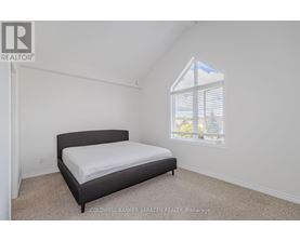 A bedroom with a bed, carpeted floor, and a window showing a view of a house and trees outside.