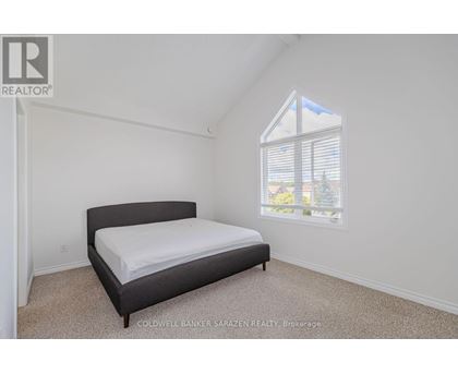 A bedroom with a bed, carpeted floor, and a window showing a view of a house and trees outside.