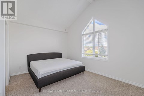 A bedroom with a bed, carpeted floor, and a window showing a view of a house and trees outside.
