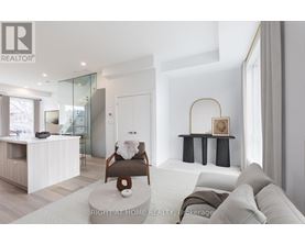 A modern living room with a glass staircase and a grey sofa.