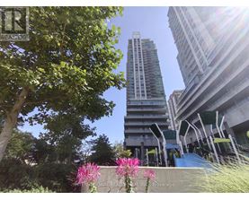 A tall building stands in the background of a sunny day with trees and flowers in the foreground.