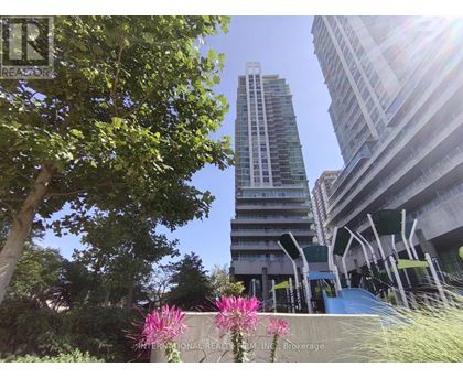A tall building stands in the background of a sunny day with trees and flowers in the foreground.