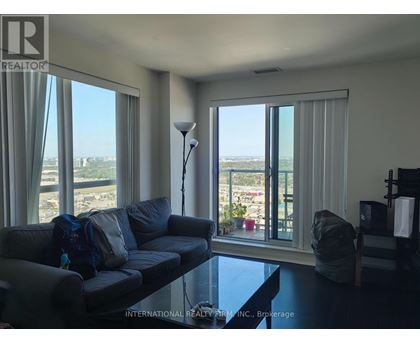 A living room with a grey couch and a view of the outside through the windows.