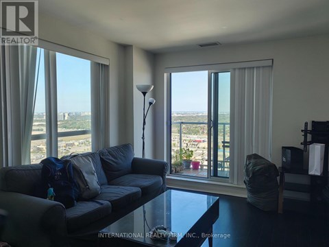 A living room with a grey couch and a view of the outside through the windows.